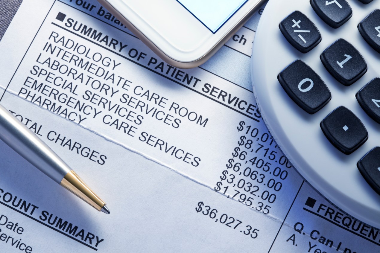 A calculator, smart phone, and a ballpoint pen rest on top of a very expensive medical bill.
