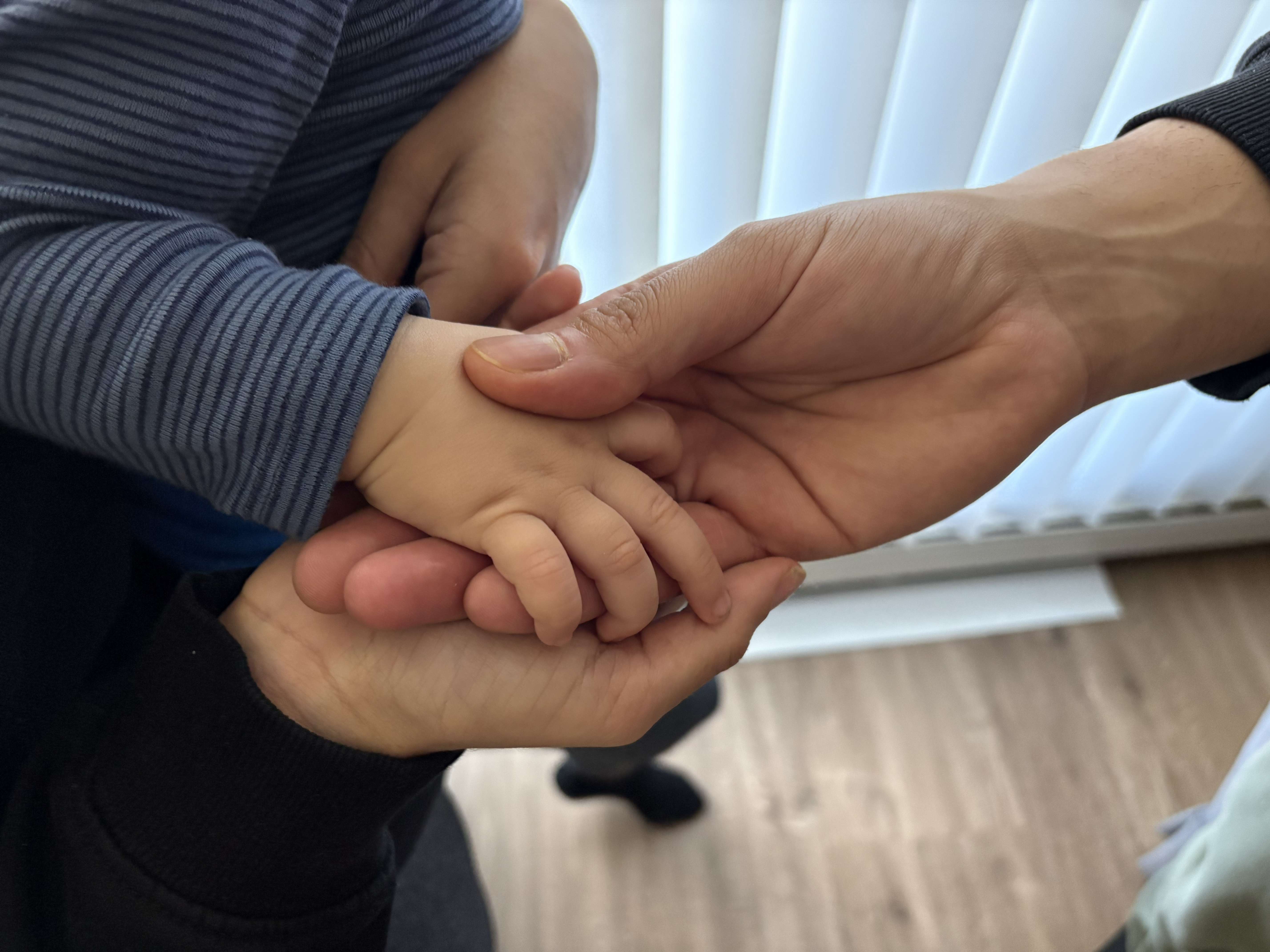 A man and a woman hold a baby's hand