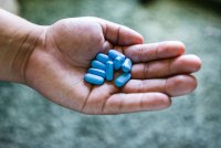 A hand holds nine light blue pills.