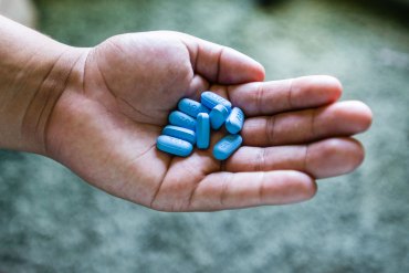 A hand holds nine light blue pills.