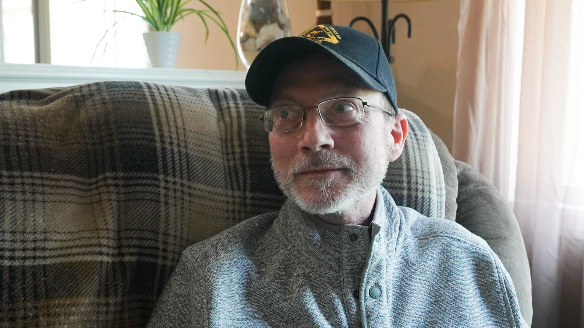 A man in a baseball cap sits in a chair.
